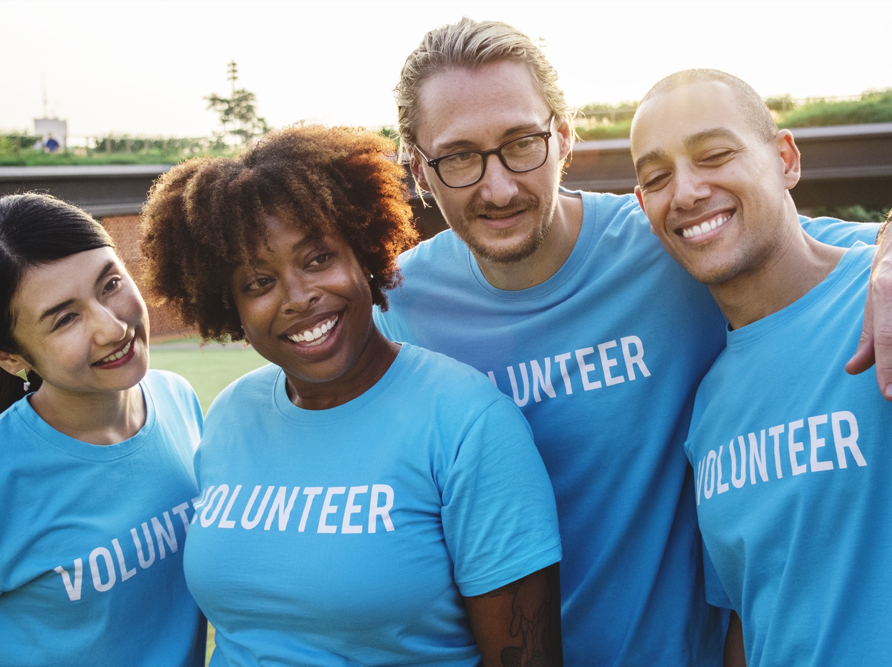 A diverse group of volunteers smiling together in volunteer shirts.